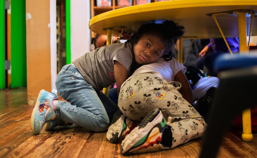 Justice Buress, 4, hides under a table while demonstrating a drill at Little Explorers Learning Center in St. Louis. Tess Trice, head of the day care program, carries out monthly drills to train the children to get on the floor when they hear gunfire.