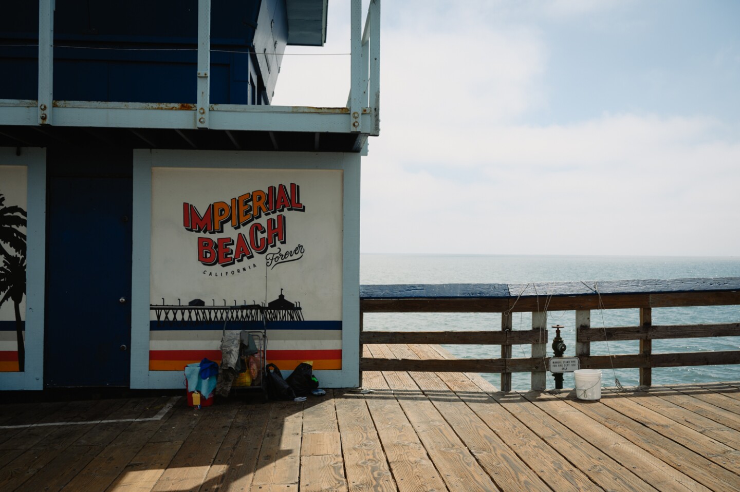 A pile of fishing gear sits beneath a colorful sign on the Imperial Beach Pier in Imperial Beach, Calif. on Sept. 3, 2024.