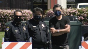 Two San Diego Police officers stand outside a parking lot next to business owner Michael Tu (right) in the Convoy District, April 8, 2021.
