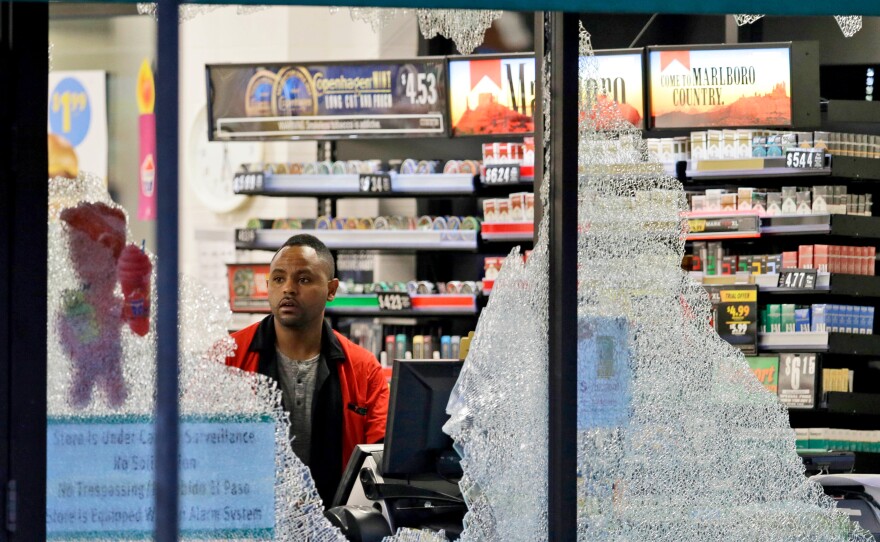 A clerk looks through broken windows, which were shot out at a convenience store in downtown Dallas.