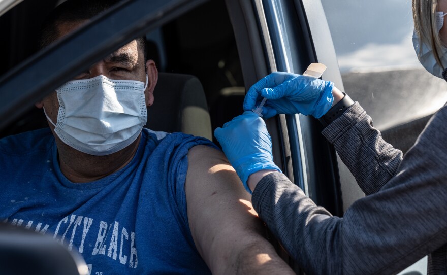 A medical professional from UofL Health administers a vaccine to a patient in their vehicle at University of Louisville Cardinal Stadium.