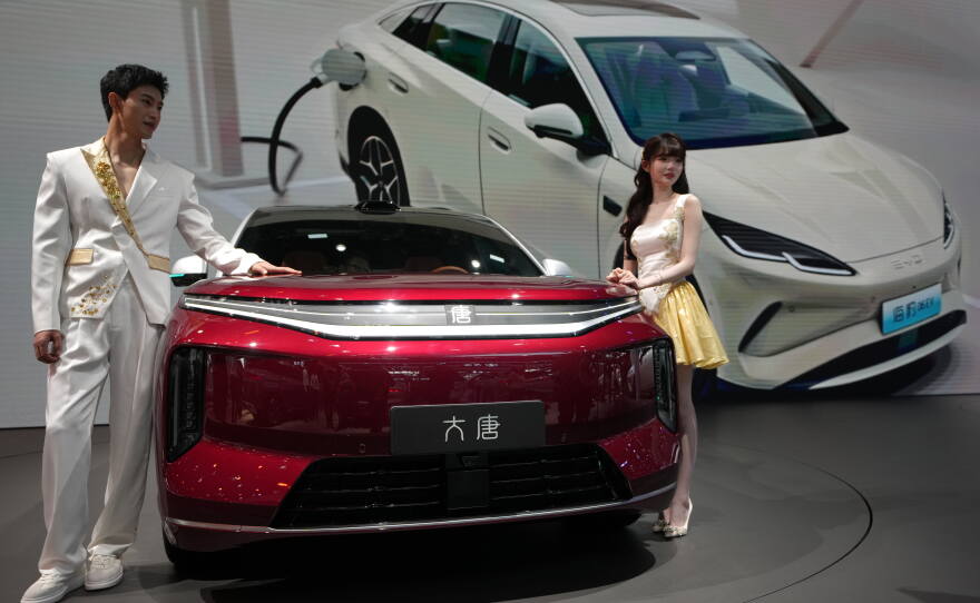 FILE - Models stand next to a latest EV car from Chinese automaker BYD showcased at the Auto China 2026, in Beijing, April 25, 2026.