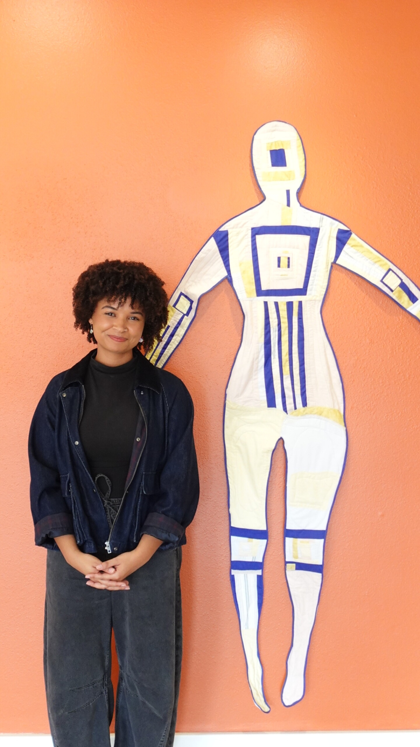 Eden DeLaVara stands in front of a quilt she made tilted "I Was Sick and in Prison," at Arts District Liberty Station on April 16, 2026.