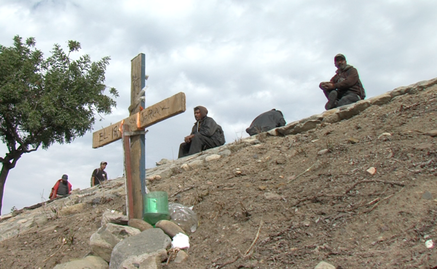 Migrants sit behind a memorial cross erected for a friend killed on the highway, Dec. 15, 2015. 