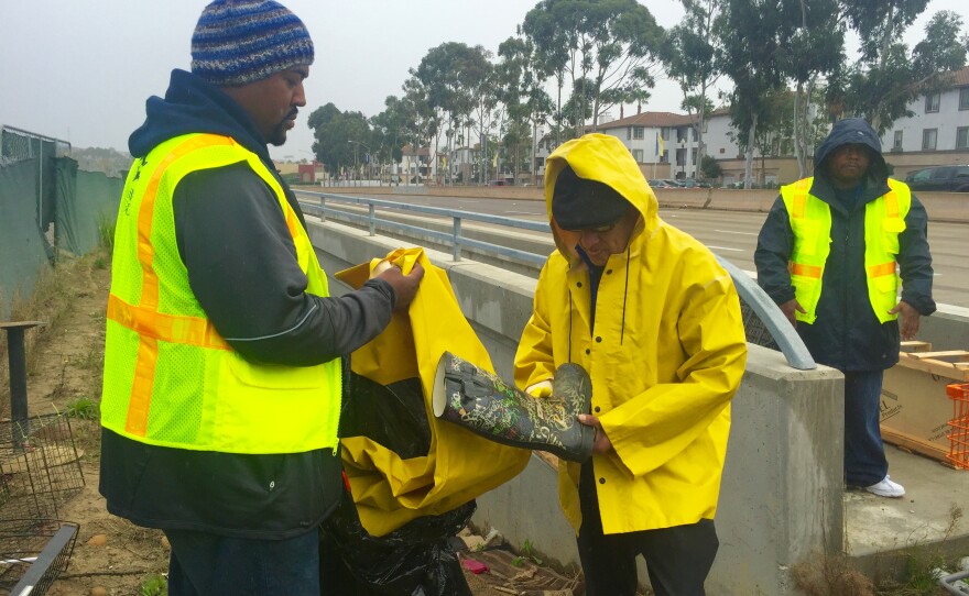 Brandon Smith (left) with the Alpha Project outreach team gives a homeless man a pair of rain boots and a rain jacket ahead of forecasted heavy rains in San Diego, Jan. 4, 2016.
