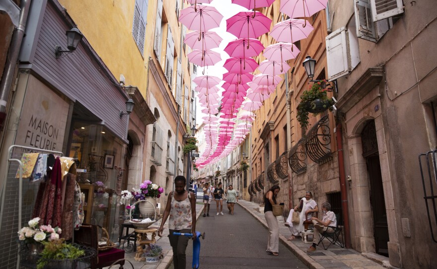 The historic center of Grasse was once home to perfume factories that have since moved out of the old town. Pink umbrellas are suspended above the streets every May through October, representing the Grasse May rose, which blooms only in May.