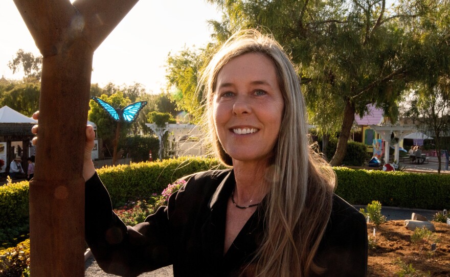 Artist Alex Heveri stands next to her sculpture at The Flower Fields at Carlsbad Ranch on March 19, 2025, while the sun illuminates another one of her sculptures in the background.
