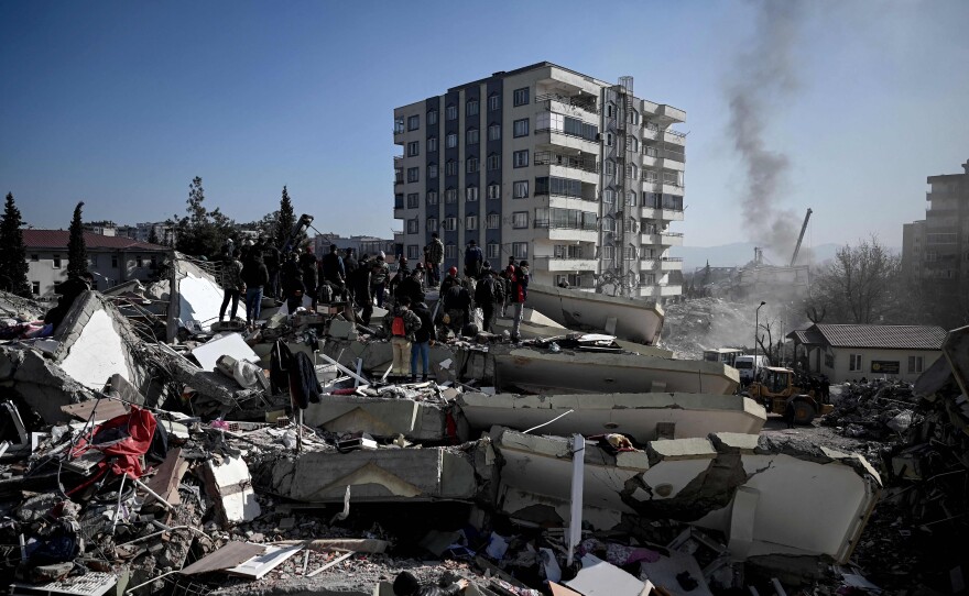 People wait as rescuers carry out search operations among the rubble of collapsed buildings in Kahramanmaras, Turkey.