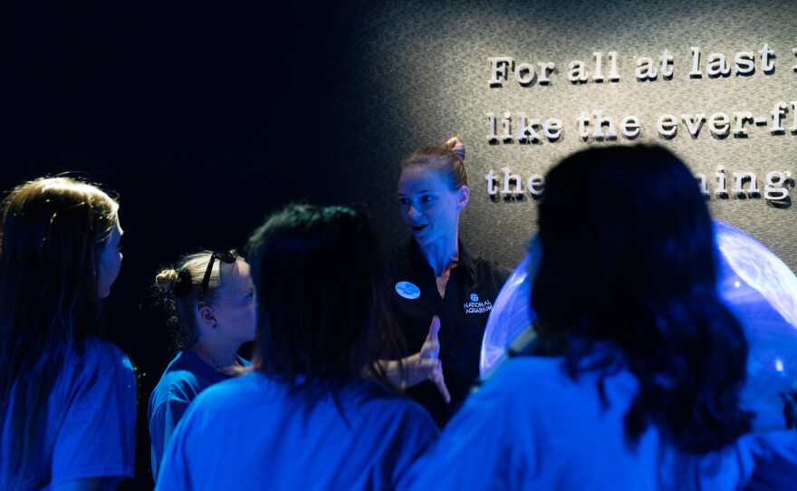 Megan Anderson, an employee of the aquarium, talks with curious visitors about a glowing globe that displays different worldwide maps, one of which show the weather. Educators at the museum talk explicitly with visitors about climate change and ways they can reduce their impact on the environment.