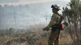 A firefighter looks onto smoke from a brush fire along I-8, June 3, 2018.