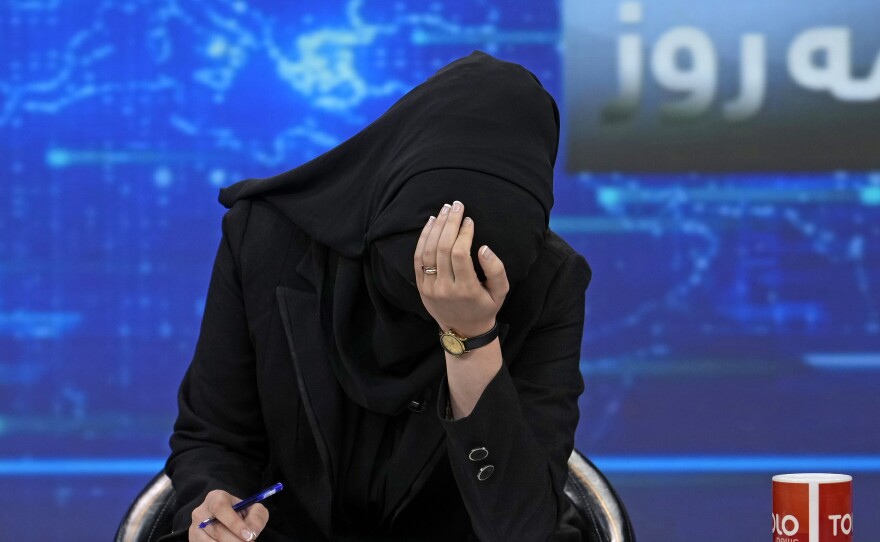TV anchor Khatereh Ahmadi bows her head while wearing a face covering as she reads the news on TOLOnews, in Kabul, Afghanistan, on Sunday. The Taliban has started enforcing an order requiring female anchors to cover their faces while on air.