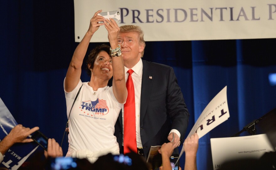 Donald Trump poses for a selfie with a woman wearing a "Team Trump" T-shirt on stage at the National Federation of Republican Assemblies Presidential Preference Convention in Nashville, Tennessee.