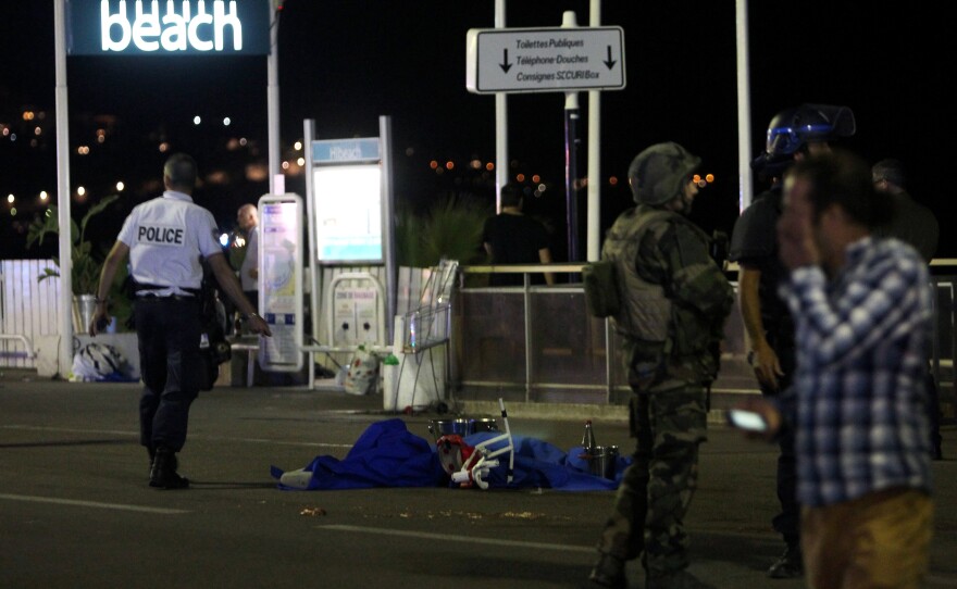 A police officer stands next to a body covered with a blue sheet on the Promenade des Anglais seafront in the French Riviera town of Nice.