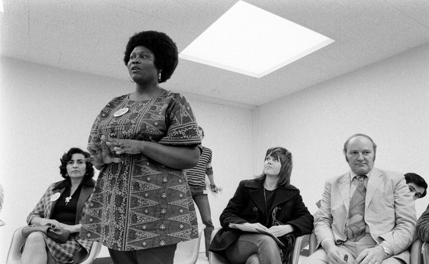 Ruby Duncan standing and addressing group, with Jane Fonda seated and listening on the eve of the Strip march in 1971.