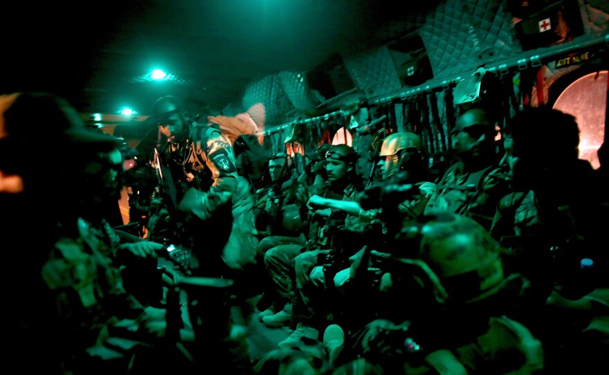 (Top) Afghan commandos on board an American Chinook helicopter flying to a Taliban-controlled village in the middle of the night. (Bottom) Commandos study a map of the village ahead of the sweep, before lining up on the tarmac to board American helicopters for the mission.