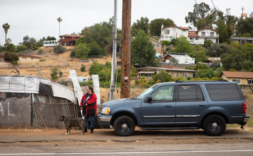Naomi Flynn stands beside her truck as traffic goes by in Spring Valley on June 7, 2021. She has been living in her truck since she was forced to leave a San Diego County run-hotel.