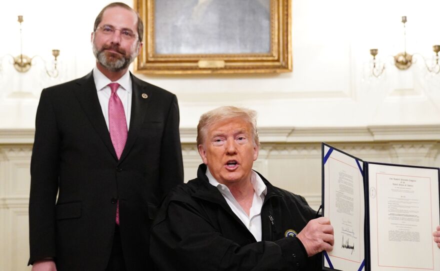 President Trump holds up the $8 billion coronavirus emergency funding bill after signing it at the White House as Health Secretary Alex Azar looks on.