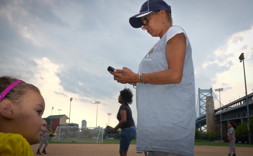 Maria Reyes, a coach for the girls Little League teams, calls players to make sure they are coming to practice at the Rutgers field.