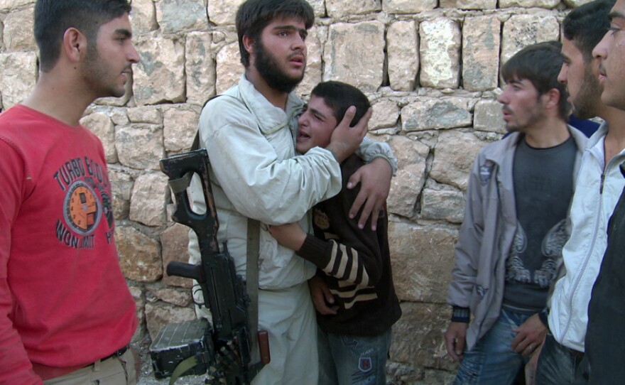 A young boy is consoled after his grandparents appear to have been killed in a government strike on the Sunni village of Al Barra.