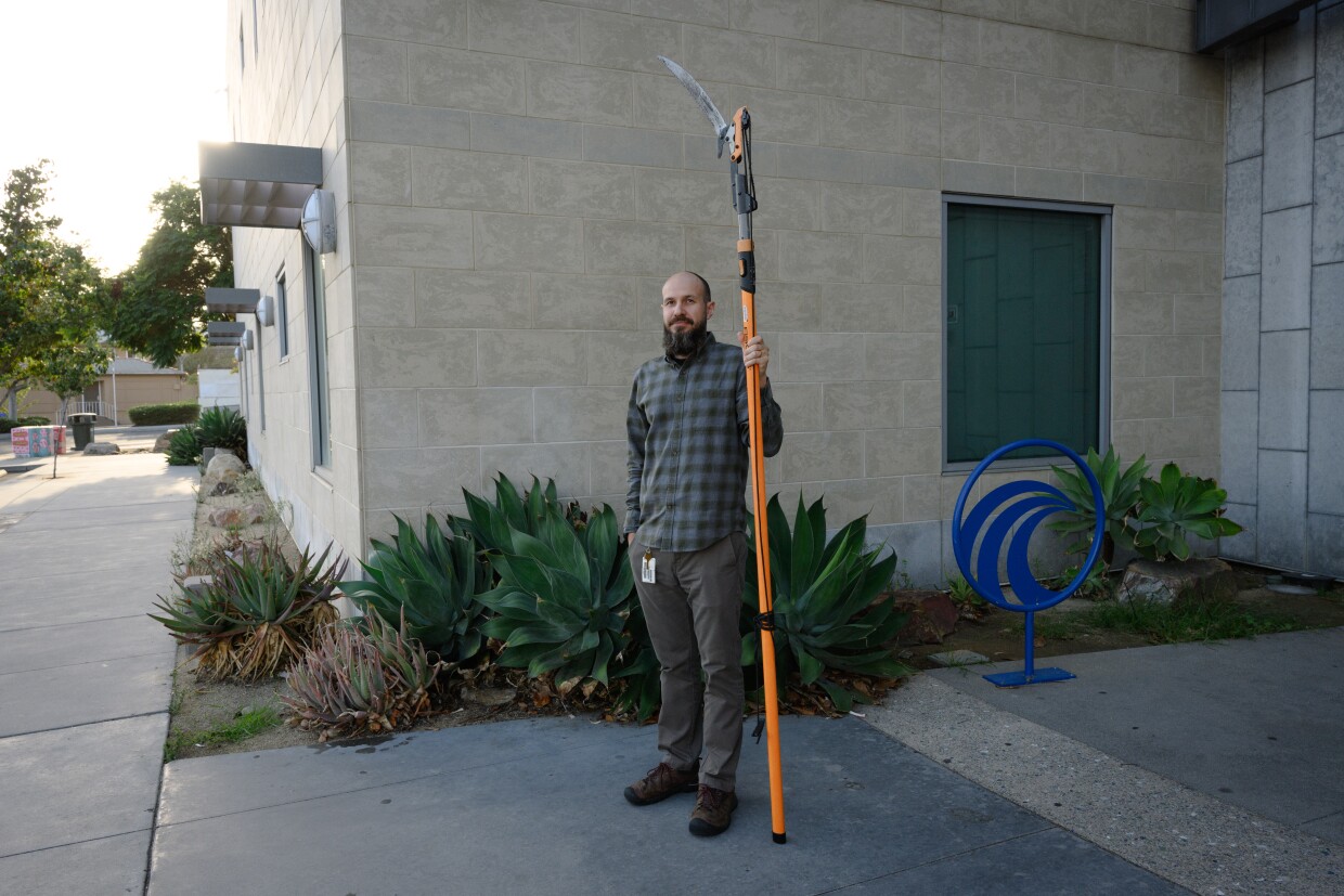 Alex Neu, an eResources and systems librarian, stands outside the National City Public Library in National City, California holding a pole saw for a portrait in October 2025. Neu runs u-Tool-ize, the library's new tool lending program.