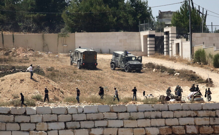 Israeli soldiers stand guard next to settlers in front of Palestinian homes that they have blockaded in the village of Qusra, south of Nablus, in the occupied West Bank, Wednesday, Aug. 12, 2026.