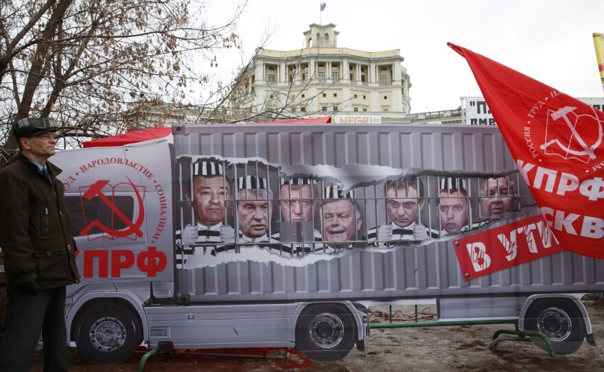 During a Dec. 5 protest against new highway fees in Moscow, a Russian Communist Party supporter stood in front of a banner with portraits of wealthy businessmen including billionaire Arkady Rotenberg, far left. Rotenberg's son, Igor Rotenberg, controls the business operating the new road fee system.