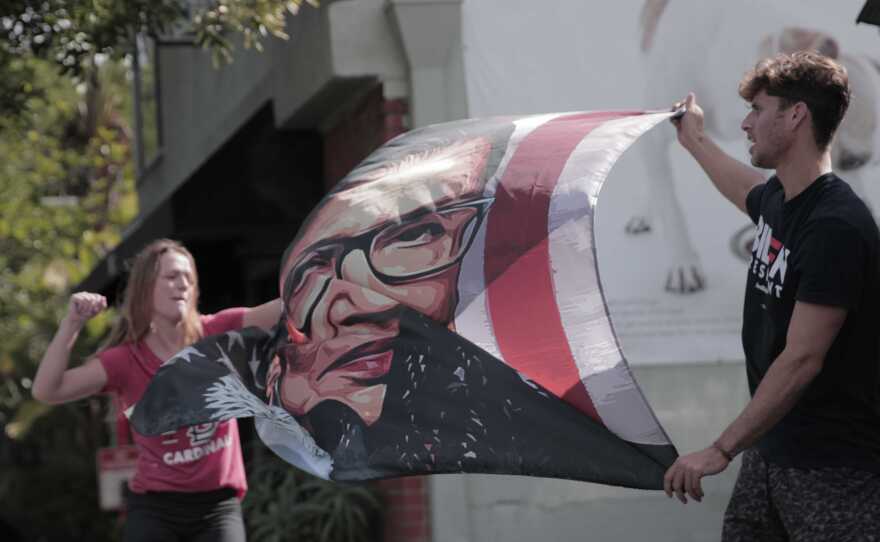 Normal Heights residents Mary Calhoun (left) and Barrett Pall (right) celebrate Biden's presidential win by waving a flag of Ruth Bader Ginsberg, in this photo taken Nov. 7, 2020.