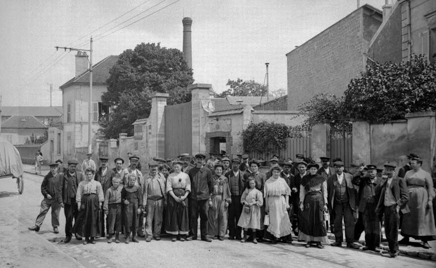 Workers stand at the exit of the Rattier factory in Bezons, France, circa 1905. Lunch pails became increasingly common at the workplace during that era in France.