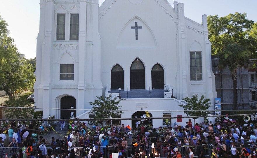 A remembrance march in memory of the Emanuel AME Church shooting victims passes a sidewalk memorial in front of the church on Saturday. The church today will hold its first Sunday service since Wednesday's shooting.