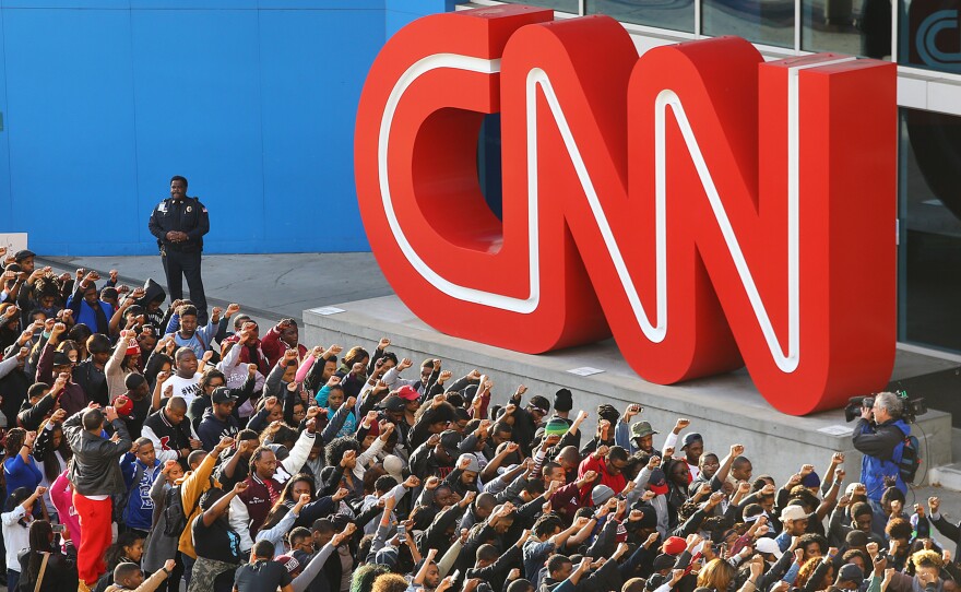 A law enforcement officer watches over Morehouse College students raising their fists in the air Tuesday, joining others in a rally at the CNN Center after marching from King's Chapel on their Atlanta campus.