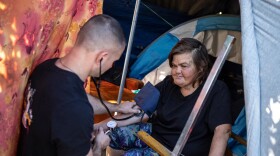 Physician assistant Brett Feldman checks Carla Bolen’s blood pressure at her encampment on the Figueroa Street Viaduct above Highway 110 in Elysian Valley Park in Los Angeles on Nov. 18, 2022.