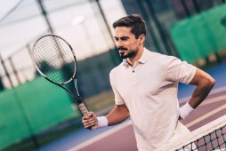 Man on tennis court. Young tennis player. Backache.