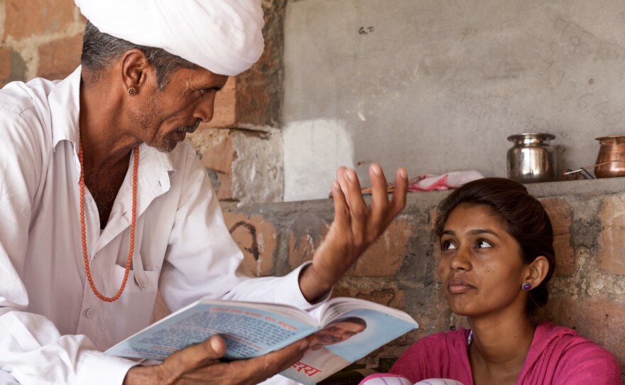 Lumbaram reads aloud to Durga from a philosophy book. Since he started his effort to rescue her from her marriage, the two have grown close.