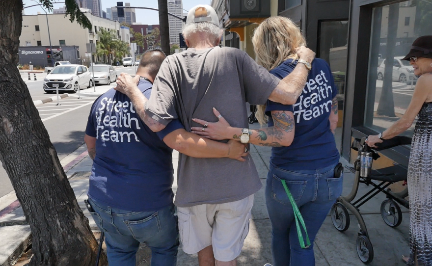 Father Joe's Villages Street Health Team outreach workers Jennifer Wilkens and Michelle LeFever help an elderly client walk in downtown San Diego on Aug. 1, 2023.