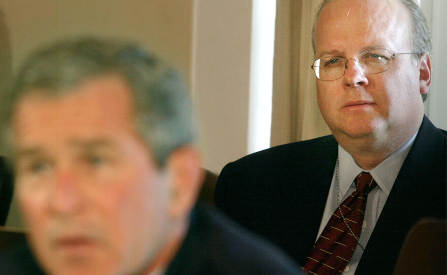 President George W. Bush (L) speaks to the news media as chief strategist, Karl Rove sits behind him, at the White House on Oct. 1, 2002. in Washington, D.C.
