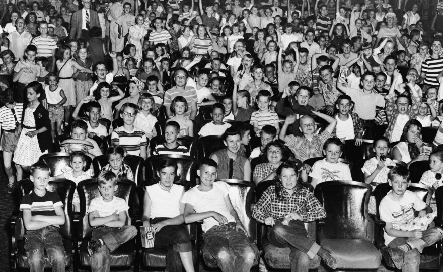 An audience of mostly children cheer and make faces in a movie theater, mid 1950s.