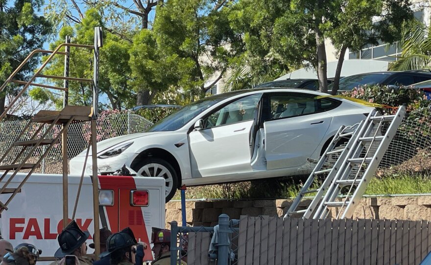 A Telsa dangling between a retaining wall and an ambulance after crashing out of a Kearny Mesa parking lot on March 30, 2021.