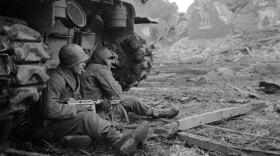 Two soldiers in Geich, Germany, pause for a cigarette behind a tank on December 11, 1944.