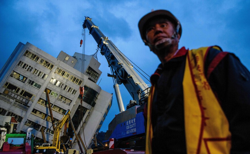 A rescue worker stands beside a wrecked, leaning building in Hualien, Taiwan, where a strong overnight earthquake leveled structures and left many survivors trapped in precarious positions.