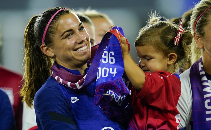 FILE -United States' Alex Morgan holds her daughter, Charlie, as she listens to Cindy Parlow Cone, president of the U.S. Soccer Federation, speak during an event with the federation, U.S. Women's National Team Players Association and the U.S. National Soccer Team Players Association at Audi Field in Washington, Tuesday, Sept. 6, 2022.