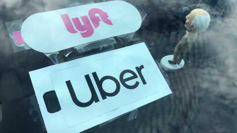 Lyft and Uber stickers and a bobblehead figurine are visible on the dashboard of a car, Nov. 5, 2020.