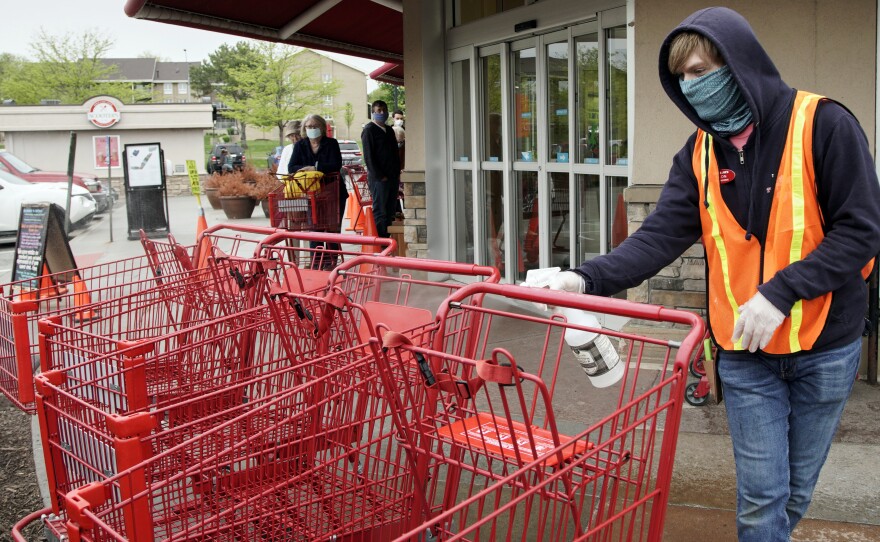 A Trader Joe's worker disinfects shopping carts and controls the number of customers allowed to shop at one time in Omaha, Neb., on May 7, 2020. Grocers like Trader Joe's are offering pay incentives to encourage their workers to get vaccinated against COVID-19.