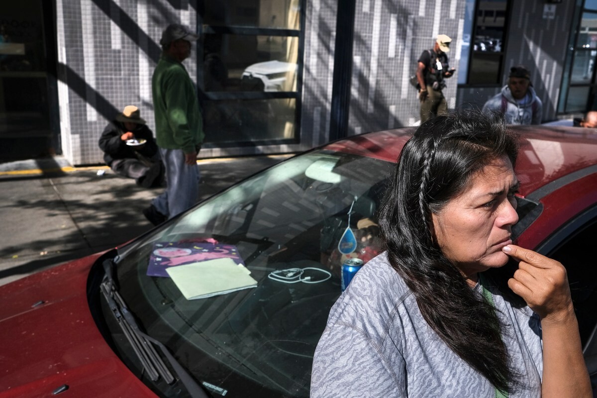 Angela Reyes Melo, 56, waits outside her car before driving to pick up supplies at a food bank on October 28, 2022, in San Diego. Reyes has been living with her son in a loaned car for the past four months.