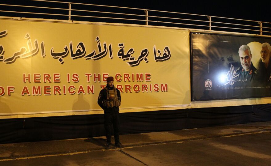 Iran is seeking to detain President Trump over the U.S. killing of top Iranian military commander Qassem Soleimani. Here, an Iraqi fighter stands in front of a banner at the site of the drone strike at Baghdad International Airport.