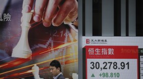 A man walks past an electronic board showing Hong Kong share index outside a local bank in Hong Kong, Wednesday, April 4, 2018. 