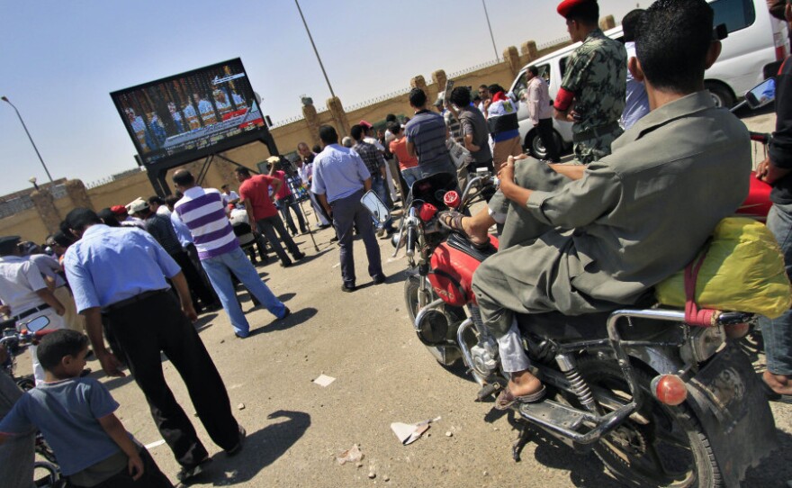 People watch the trial of former Egyptian Interior Minister Habib el-Adly and six top police officials live on a TV screen outside the Police Academy complex in Cairo, Egypt Thursday, Aug. 4, 2011. A day after the start of Hosni Mubarak's trial, seven of his co-defendants are back in the courtroom on charges of ordering the killing of protesters during uprising that toppled Egypt's president.
