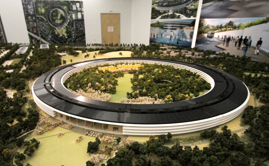 A scale model of the completed campus shows the plan for a solar panel roof atop a futuristic-looking four-story glass and concrete building. Rolling hills, walking paths and trees will comprise 80 percent of the site, Apple says.