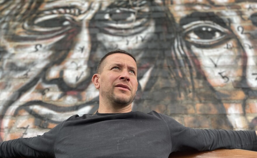 Vladyslav Krasnoshchok sits in front of one of the many murals he's painted in his garden outside his home in Kharkiv, Ukraine.