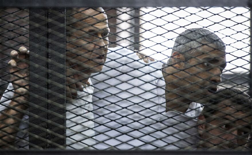 Australian journalist Peter Greste (left) of Al-Jazeera news channel and his colleagues, Egyptian-Canadian Mohamed Fadel Fahmy (center) and Egyptian Baher Mohamed, listen to the verdict inside the defendants' cage during their trial for allegedly supporting the Muslim Brotherhood.