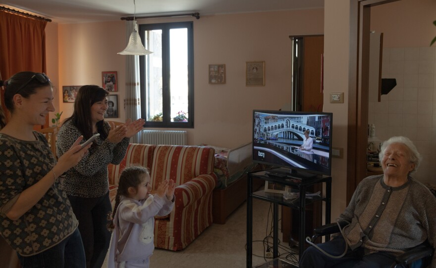 Khrystyna Mala, Lyubov Mala and Milana Dorosh applaud photographer Chiara Negrello's grandmother Lidia as she pushes her wheelchair by herself for the first time since returning home from the hospital in April 2022. Lidia was thin, breathing poorly, unable to feed herself and bedridden when she returned from the hospital. Lyubov helped Lidia improve so she could accomplish small tasks on her own.